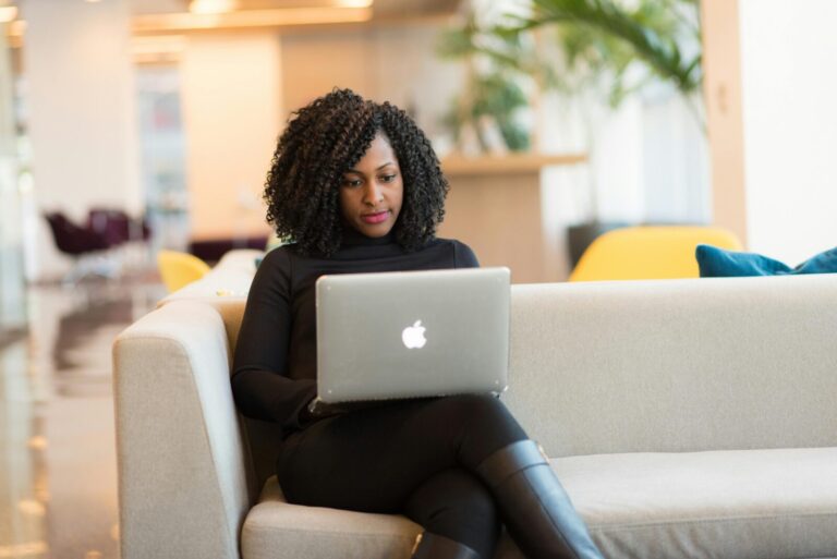 A confident Black woman in a sunny room with a laptop on a sofa.