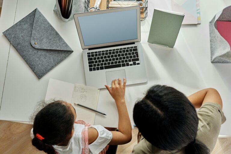 Overhead view of a young Black girl and a female mentor or parent using a laptop together in a bright workspace