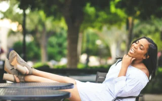 Black woman relaxing outdoors at a café table with her feet up, smiling joyfully in soft natural light